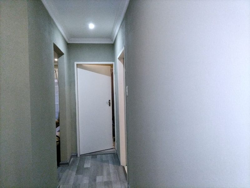 A clean, well-lit hallway featuring modern laminate flooring, neutral wall finishes, and recessed ceiling lighting connecting to adjacent rooms.