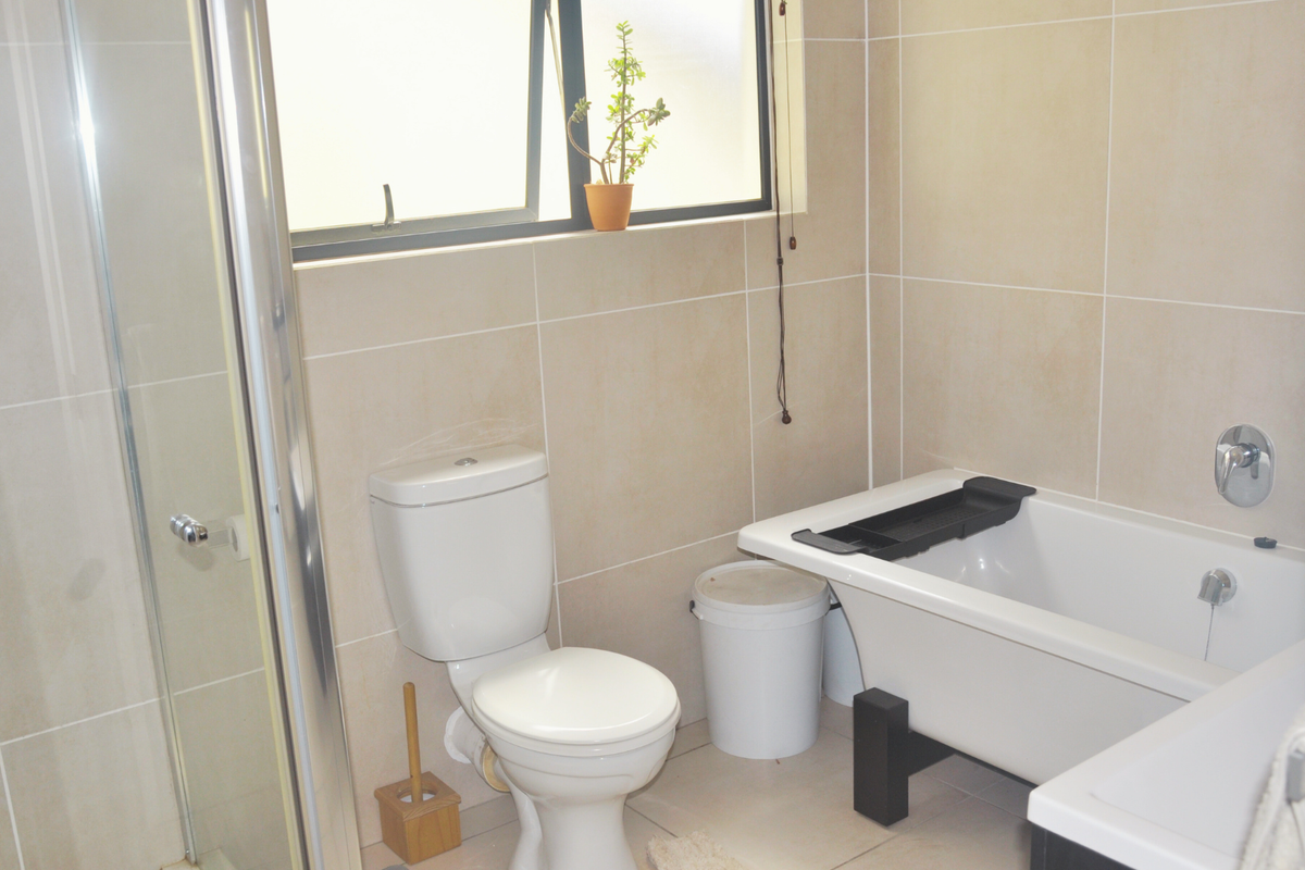 A functional bathroom featuring a shower enclosure, a bathtub, and a toilet with neutral wall and floor tiling.