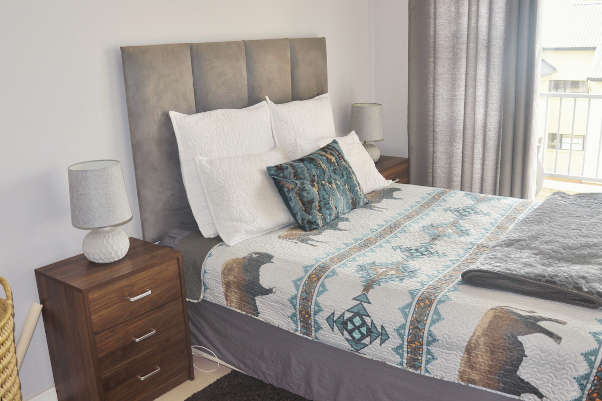 A well-maintained bedroom featuring a neutral color palette, direct access to a private balcony through a sliding glass door, and ample natural light.