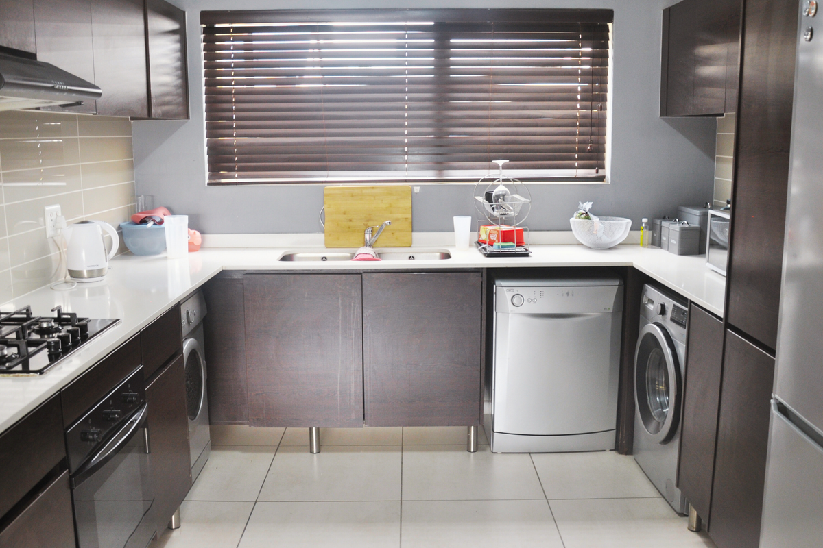 Modern kitchen featuring dark wood cabinetry, white quartz countertops, gas hob, extractor fan, built-in oven, and integrated space for laundry appliances.