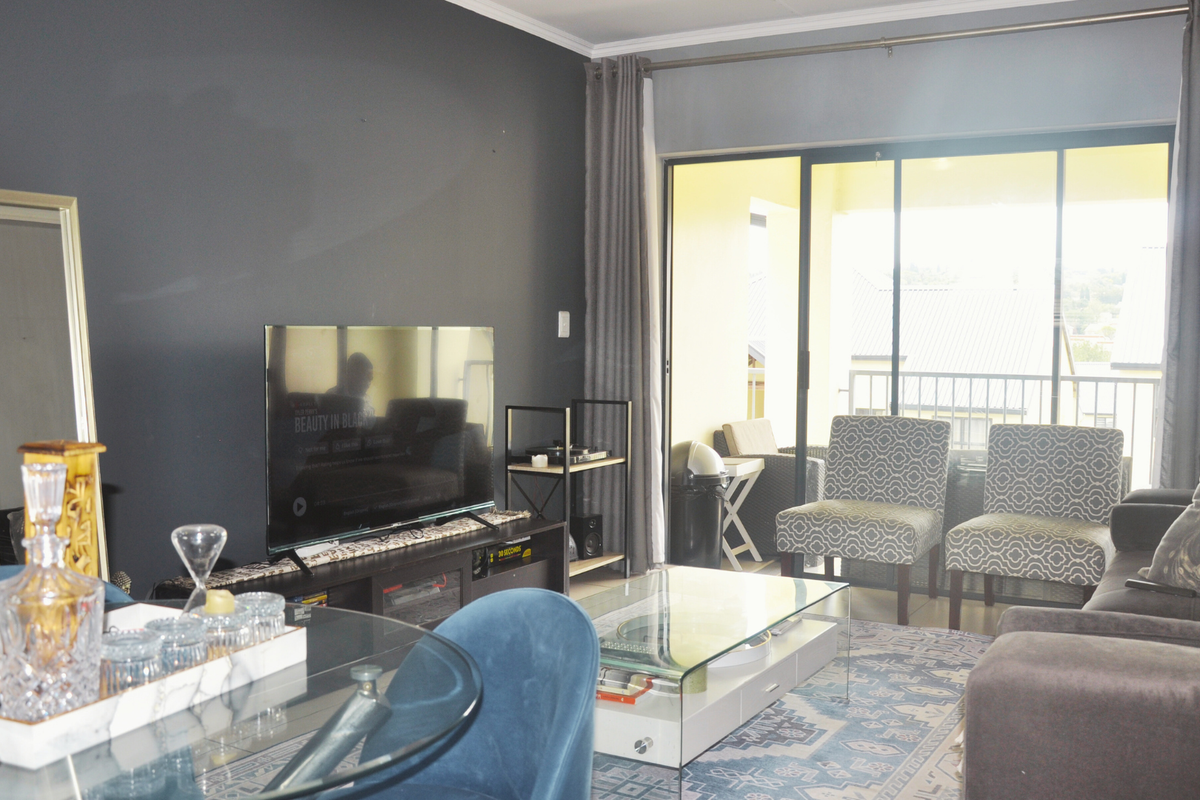 A well-maintained living room featuring a dark accent wall, large sliding glass doors leading to a balcony, and neutral flooring.