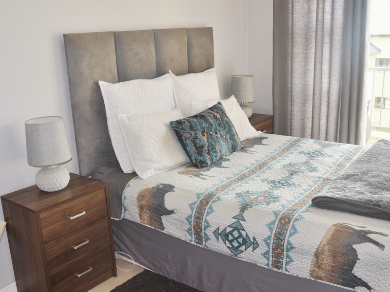 A well-maintained bedroom featuring a neutral color palette, direct access to a private balcony through a sliding glass door, and ample natural light.