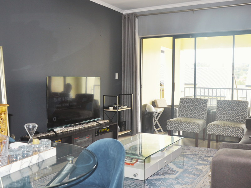 A well-maintained living room featuring a dark accent wall, large sliding glass doors leading to a balcony, and neutral flooring.