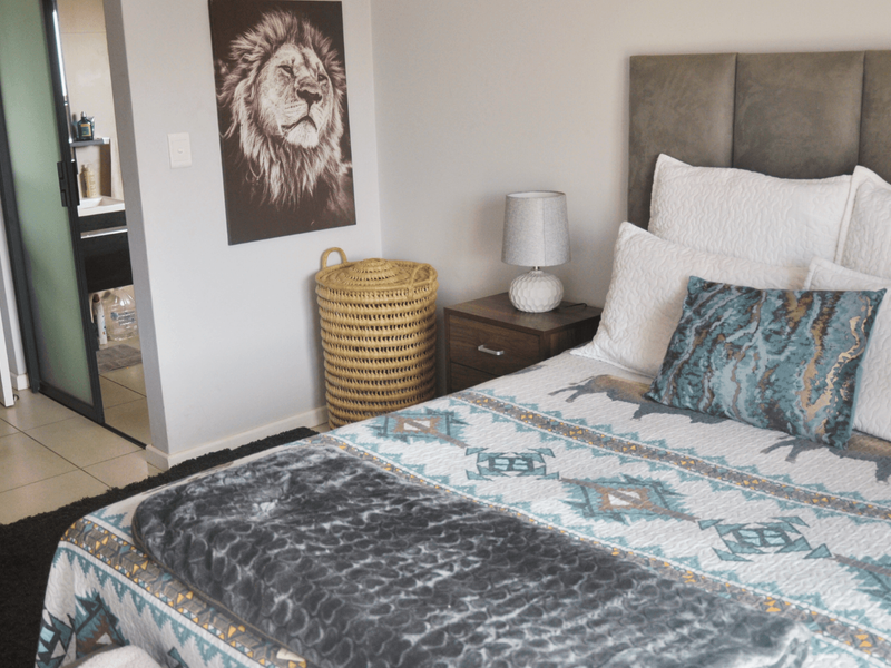 A well-maintained bedroom featuring a modern upholstered headboard, neutral wall finishes, and tiled flooring, with an adjacent en-suite bathroom visible through a sliding door.