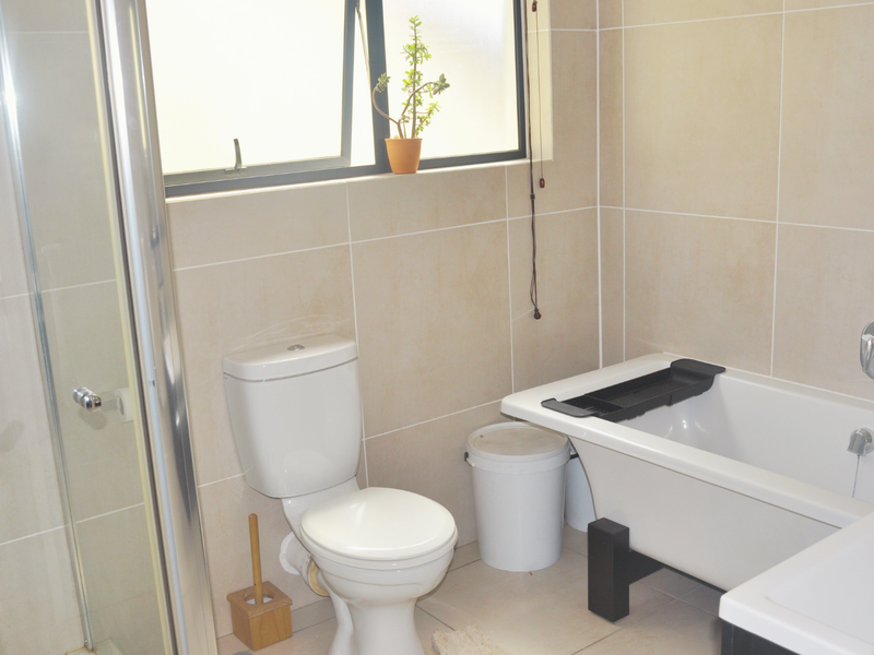 A functional bathroom featuring a shower enclosure, a bathtub, and a toilet with neutral wall and floor tiling.