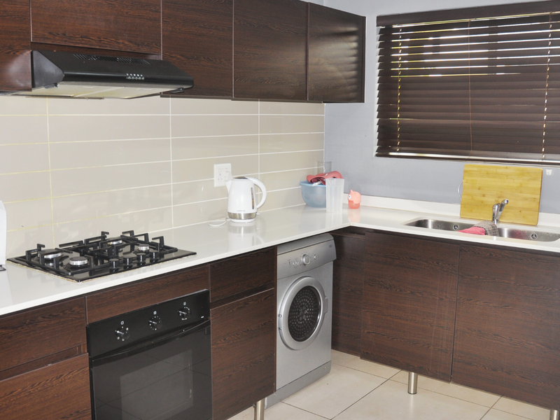 Modern kitchen featuring dark wood cabinetry, white stone countertops, integrated gas hob, built-in oven, and a double bowl sink with a tiled backsplash.