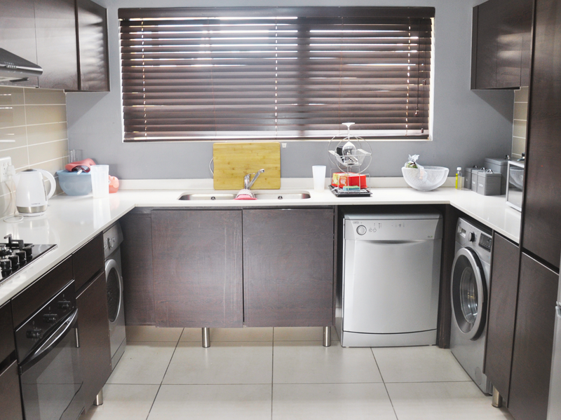 Modern kitchen featuring dark wood cabinetry, white quartz countertops, gas hob, extractor fan, built-in oven, and integrated space for laundry appliances.