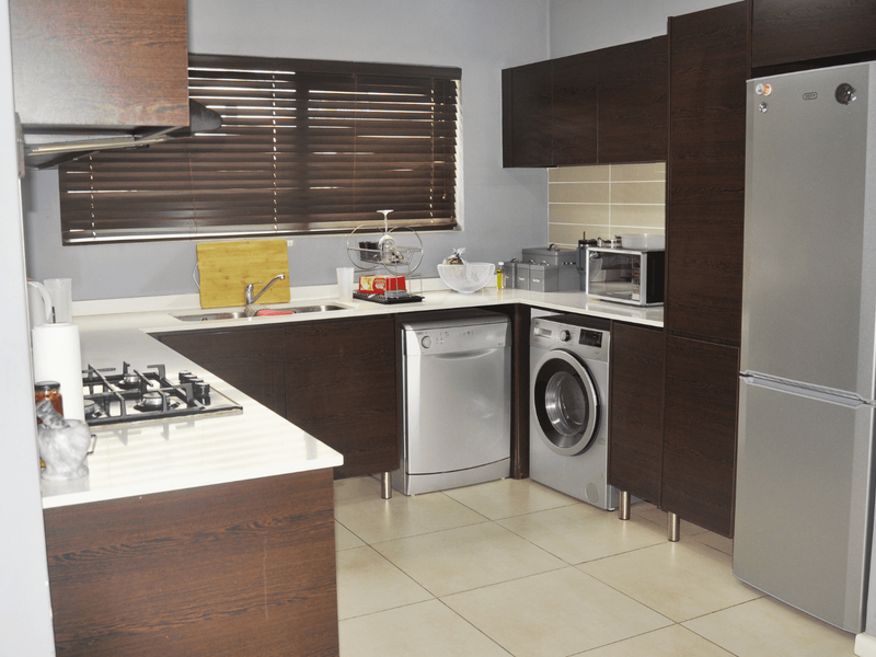 Modern kitchen featuring dark wood cabinetry, stone countertops, gas hob, and integrated space for appliances, finished with neutral tiled flooring and venetian blinds.