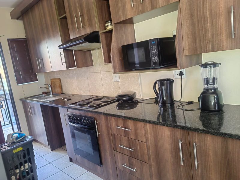 A functional kitchen featuring wood-look laminate cabinetry, granite countertops, a built-in oven with electric hob, and a tiled backsplash.
