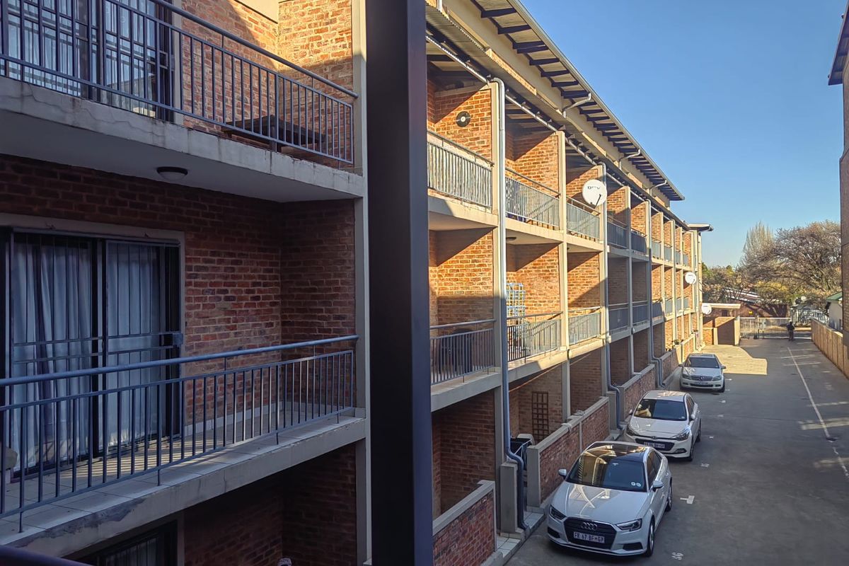 Exterior view of a multi-story apartment complex featuring exposed brick facades, concrete balconies with metal railings, and a paved parking area.