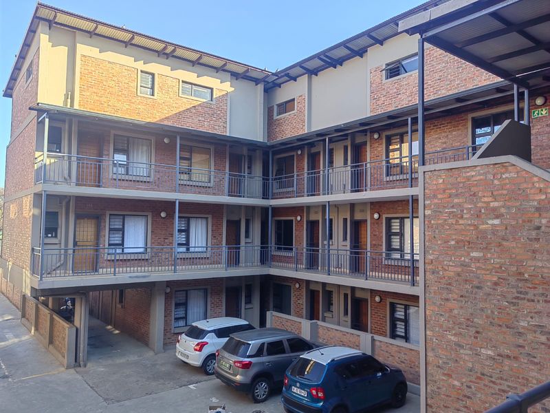A multi-story apartment complex featuring face brick exterior walls, metal balcony railings, and covered walkways with ground-level parking.
