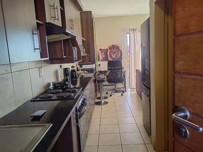 A functional galley-style kitchen featuring dark wood cabinetry, granite countertops, and integrated appliances, leading into a small adjacent living or workspace area.