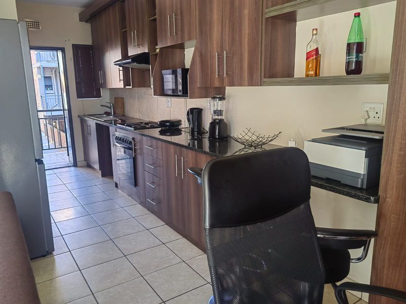 A functional kitchen featuring dark wood cabinetry, granite countertops, built-in oven and hob, and direct access to an outdoor balcony area.