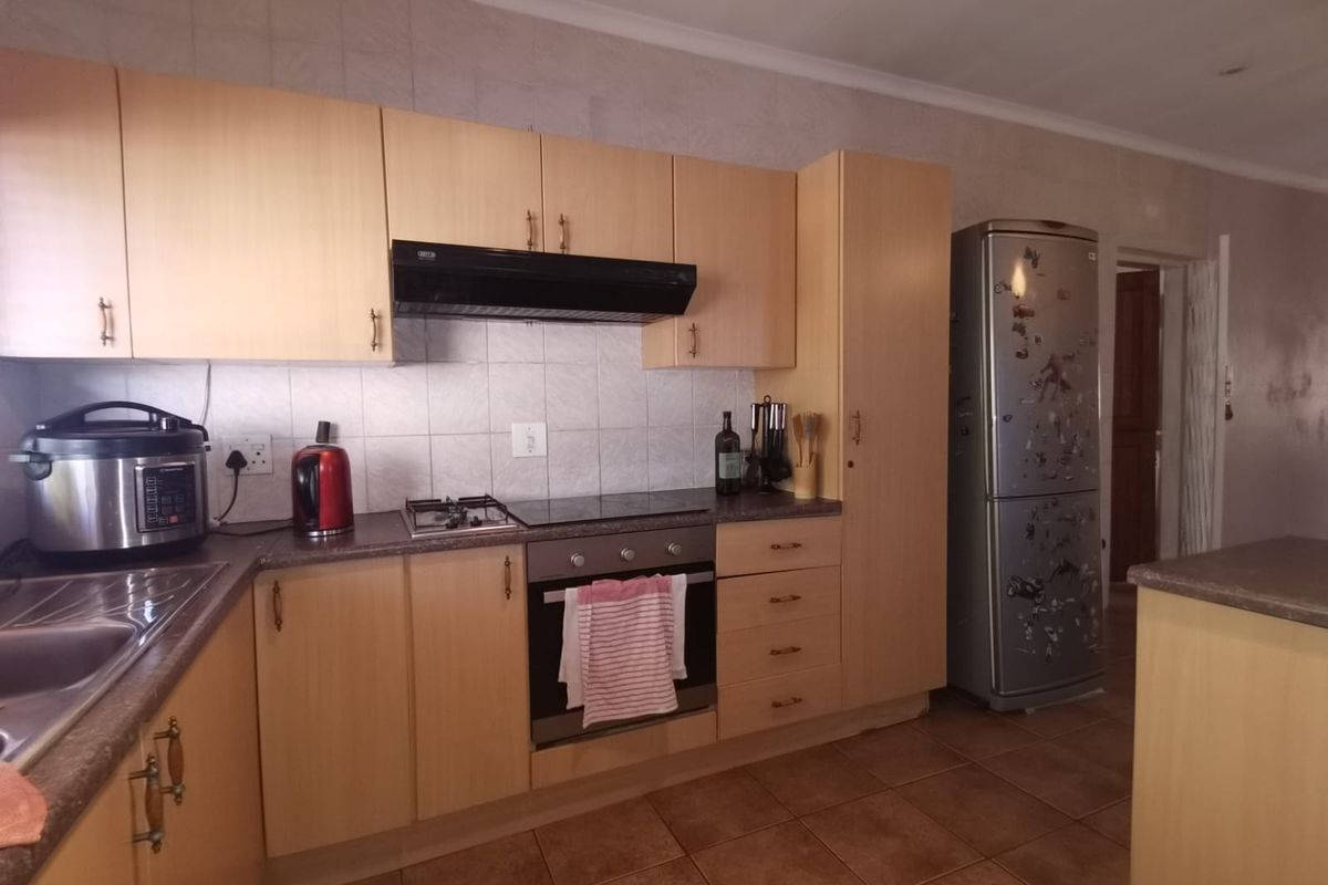 A functional kitchen featuring light wood-look cabinetry, built-in oven and hob, tiled splashbacks, and durable floor tiles, offering a practical layout for daily use.
