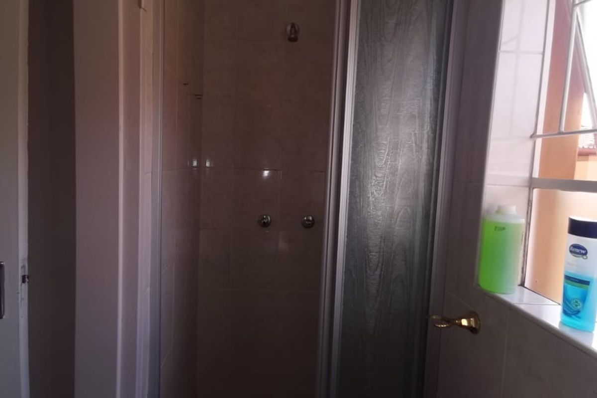 A functional bathroom featuring a shower enclosure with tiled walls and a wall-mounted basin, offering a standard layout for a townhouse.