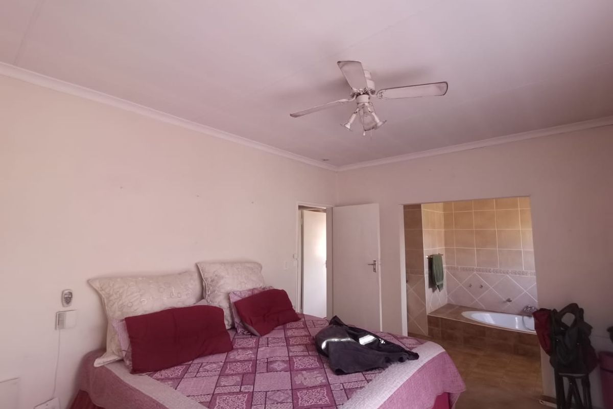 A bedroom featuring a ceiling fan and an open-plan en-suite bathroom with a built-in bathtub and tiled finishes.
