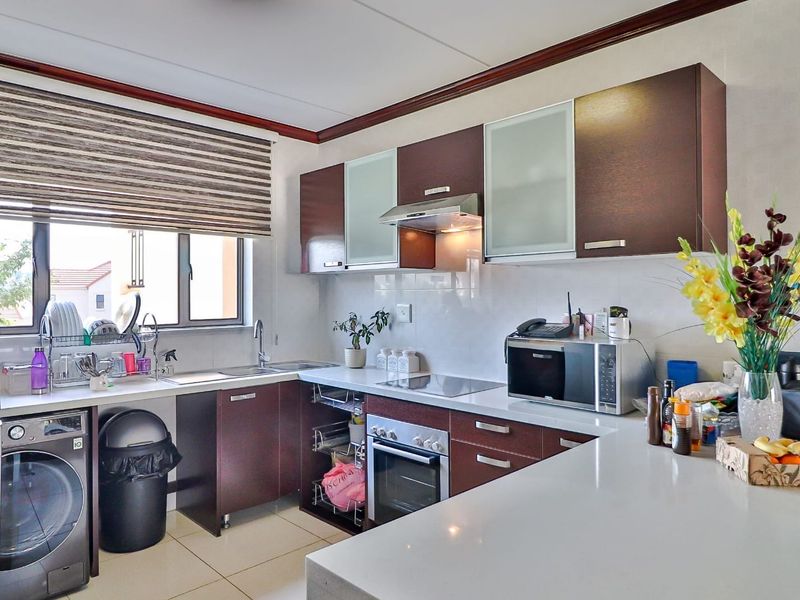 A functional kitchen featuring dark wood cabinetry, stone countertops, a built-in oven, hob, extractor fan, and integrated space for a washing machine.