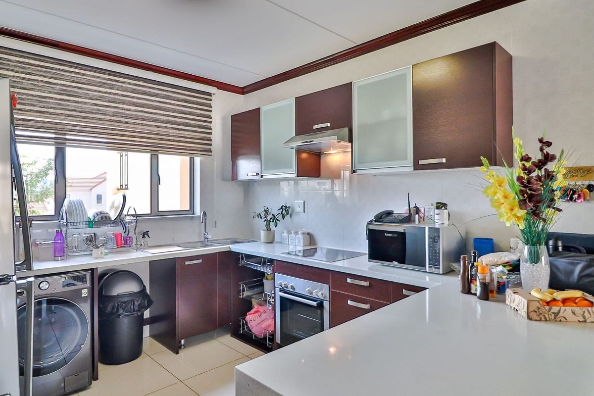 A functional kitchen featuring dark wood cabinetry, stone countertops, a built-in oven, hob, extractor fan, and integrated space for a washing machine.
