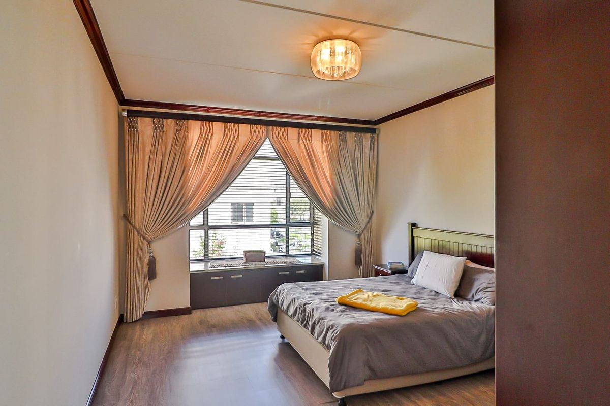 A well-maintained bedroom featuring wood-look flooring, a large window with built-in storage cabinetry, and crown molding.