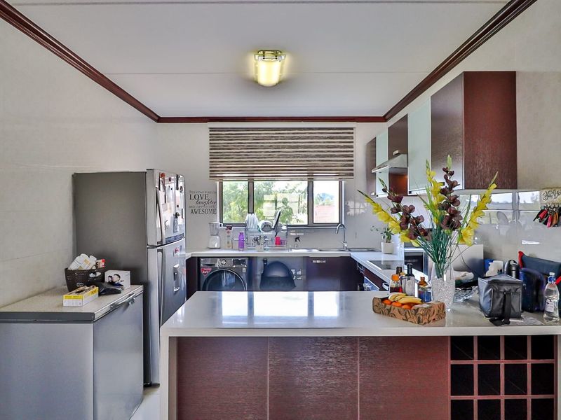 A functional kitchen featuring dark wood cabinetry, a central island with integrated wine rack, stainless steel sink, and tiled splashbacks.