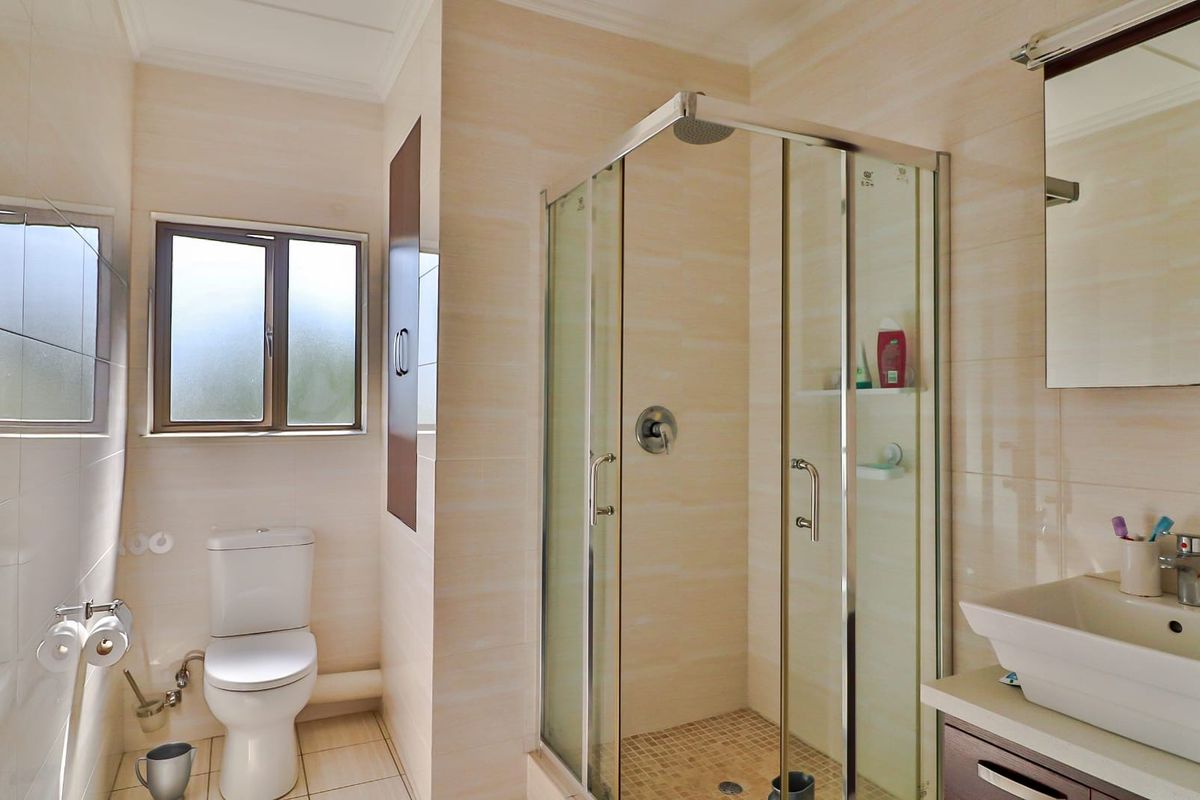 A well-maintained bathroom featuring a glass-enclosed shower, a modern vanity basin, and a standard toilet with tiled walls and flooring.