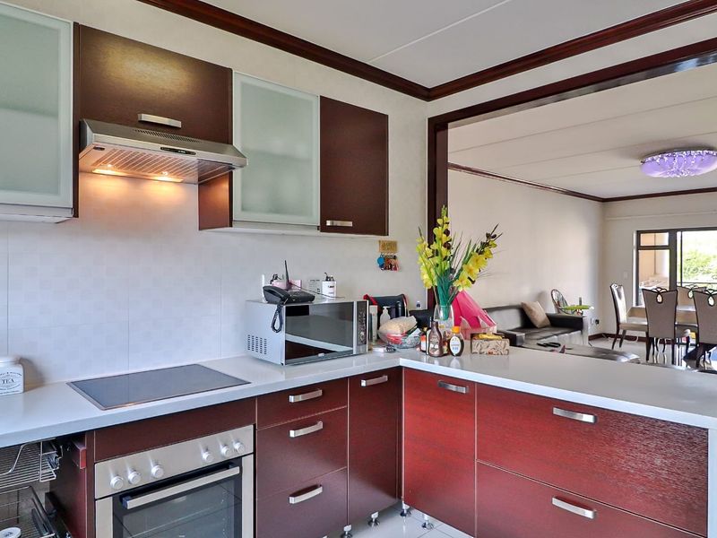 A functional kitchen featuring dark wood cabinetry, a built-in oven, electric hob, and extractor fan, flowing into an open-plan living and dining area.