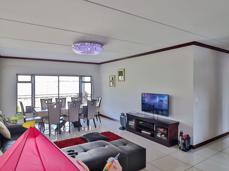 An open-plan living and dining area featuring tiled flooring, large sliding glass doors leading to a balcony, and a decorative ceiling light fixture.
