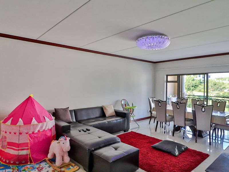 Spacious open-plan living and dining area featuring tiled flooring, a decorative ceiling light fixture, and large sliding glass doors leading to a balcony.