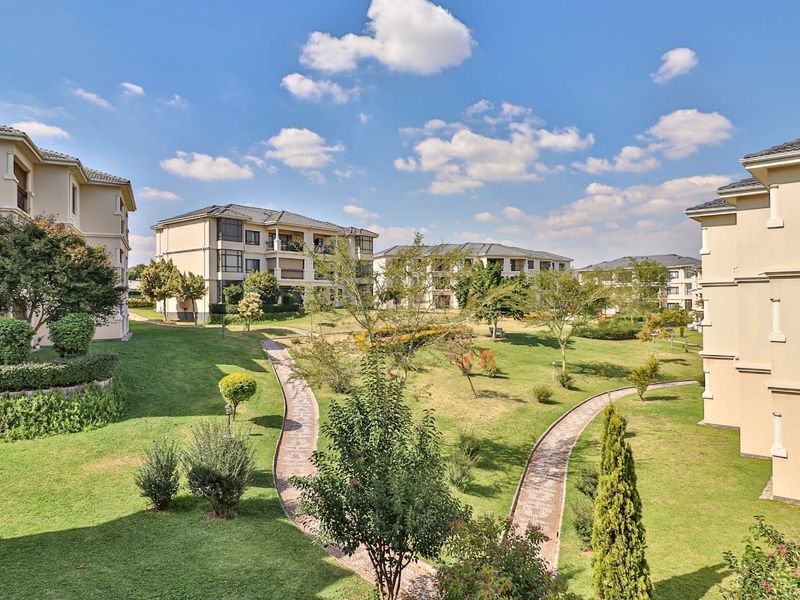 A view of the well-maintained communal garden area featuring landscaped lawns, paved pathways, and surrounding apartment building facades.