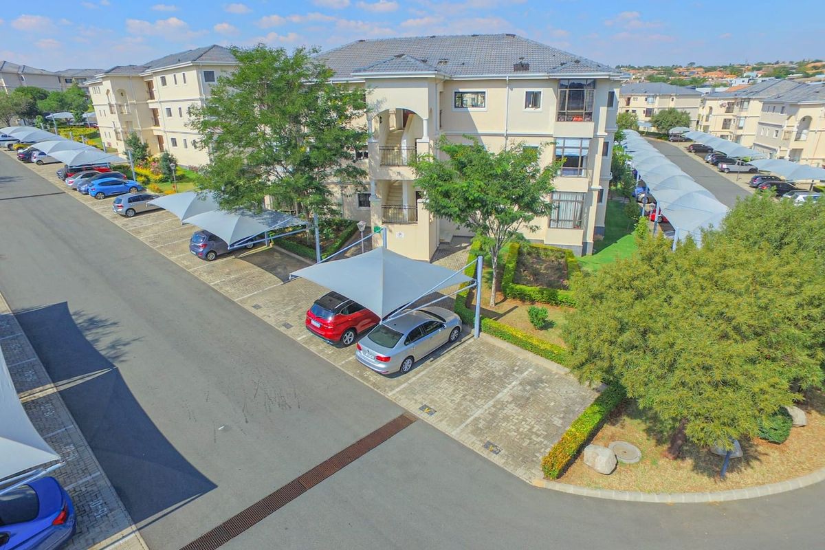 Aerial view of the apartment complex featuring paved parking areas with shade-cloth carports and landscaped garden surrounds.