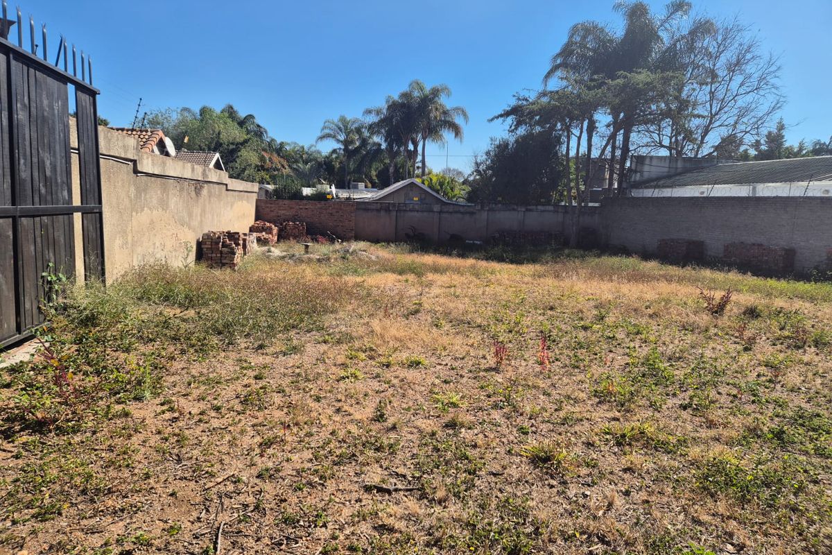 A vacant residential plot enclosed by perimeter walls and a metal gate, featuring open ground with natural vegetation.