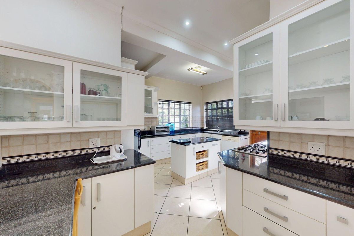A functional kitchen featuring white cabinetry, granite countertops, a central island, and tiled flooring with a classic layout.