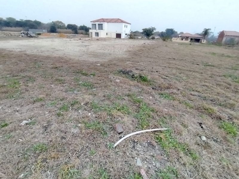 A view of a vacant residential plot of land with surrounding neighborhood properties visible in the distance.