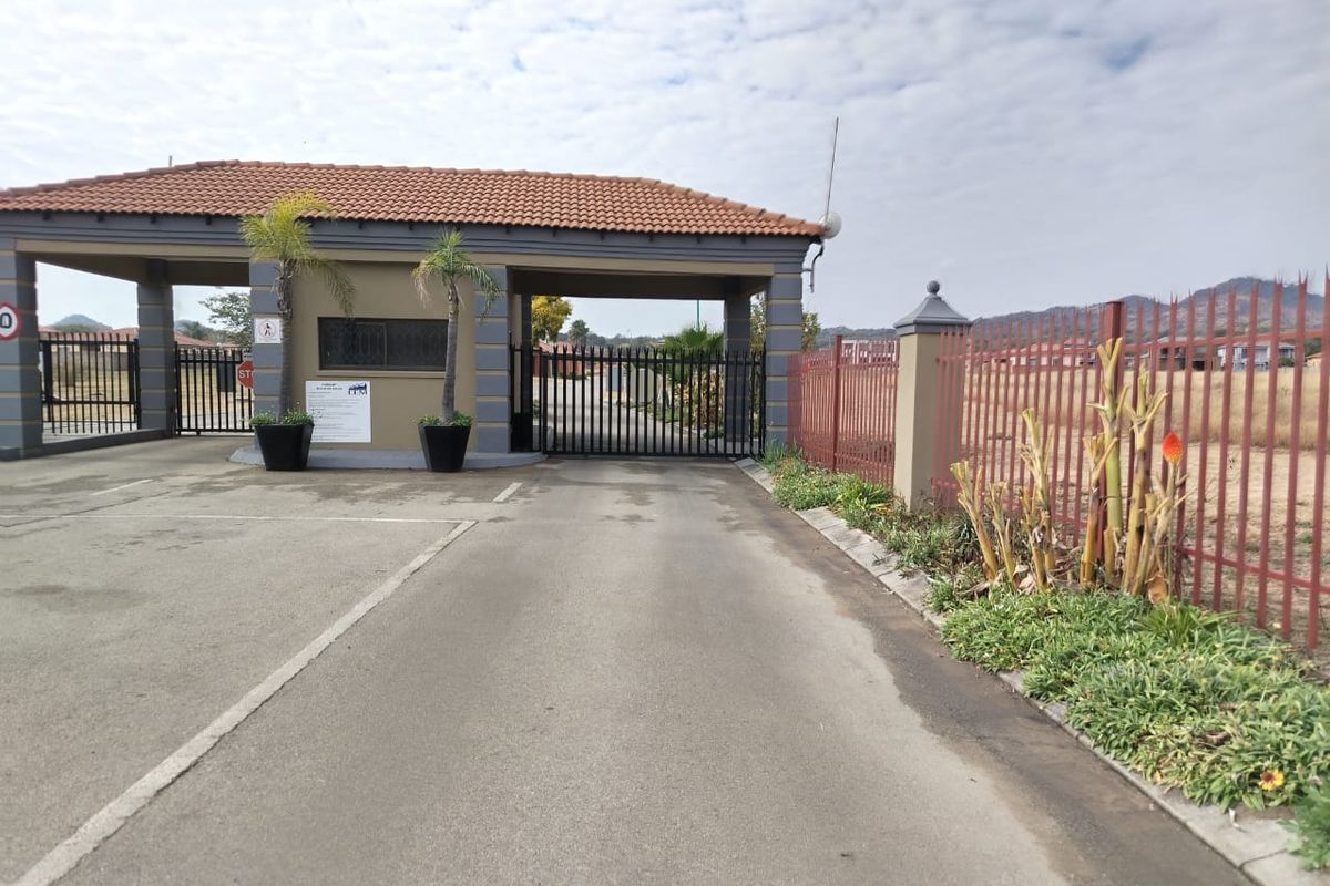 A secure gated entrance to a residential estate featuring a guardhouse, paved driveway, and perimeter metal fencing.
