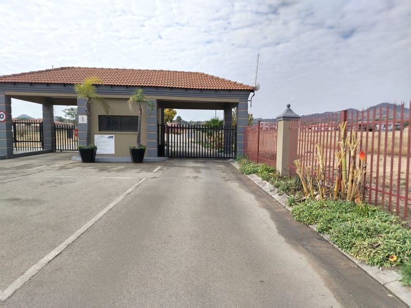 A secure gated entrance to a residential estate featuring a guardhouse, paved driveway, and perimeter metal fencing.