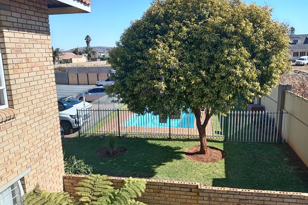 Elevated view of a private rear garden featuring a swimming pool, established tree, and secure perimeter fencing with brick boundary walls.