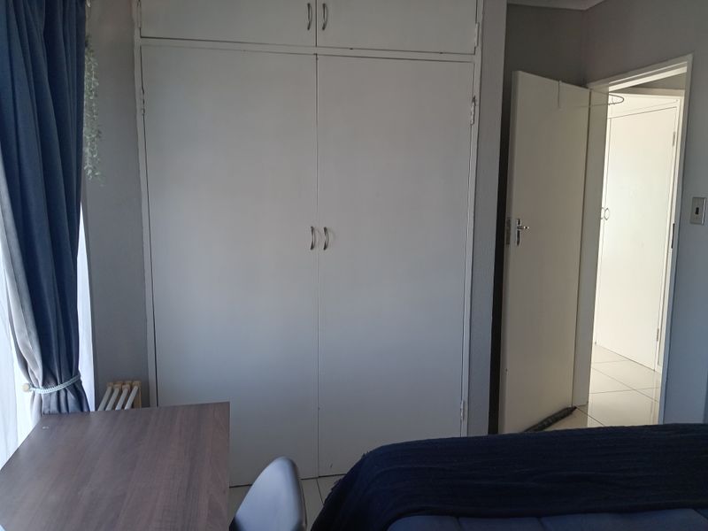 A bedroom featuring built-in cupboards with overhead storage, tiled flooring, and access to an adjoining room.