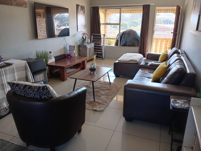 A spacious living room featuring large windows, tiled flooring, and direct access to an outdoor patio area.