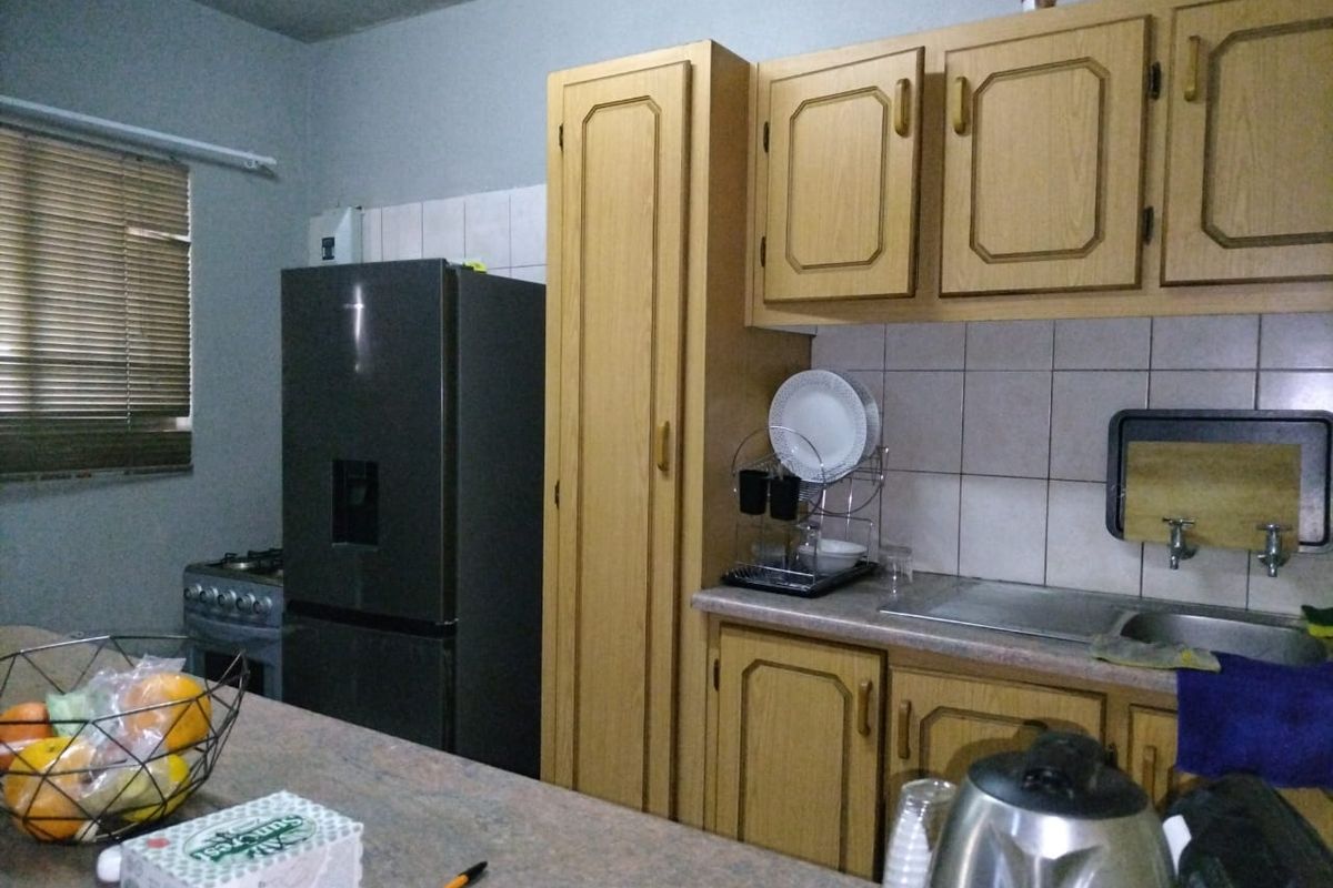 A functional kitchen featuring wooden cabinetry, tiled backsplash, laminate countertops, and a stainless steel sink, offering a practical layout for daily meal preparation.