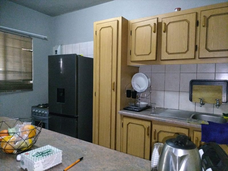A functional kitchen featuring wooden cabinetry, tiled backsplash, laminate countertops, and a stainless steel sink, offering a practical layout for daily meal preparation.
