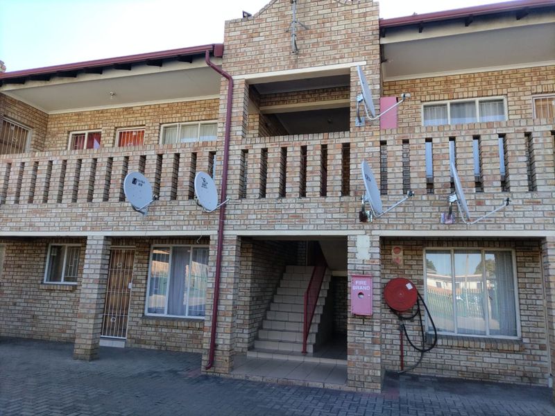 A two-story face brick apartment building featuring external staircases, balconies, and communal fire safety equipment with paved driveway access.