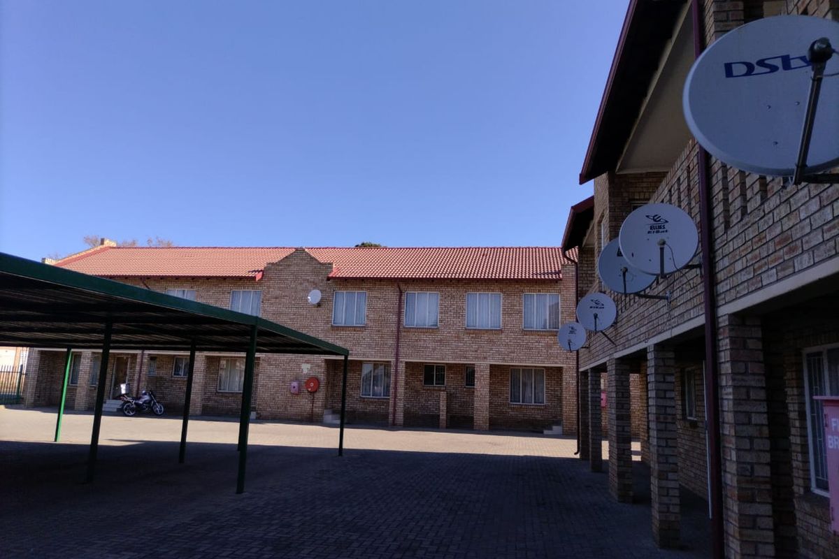 Rear view of a face brick apartment complex featuring a paved courtyard area and covered parking bays.