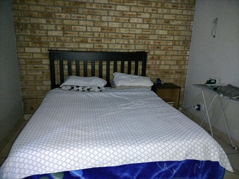 A bedroom featuring an exposed brick feature wall and tiled flooring, requiring minor electrical finishing to address exposed wiring.