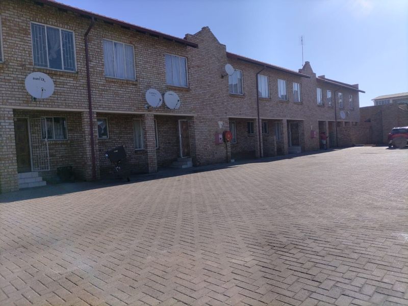 Exterior view of a multi-unit face-brick residential complex featuring a paved driveway and secure unit entrances.