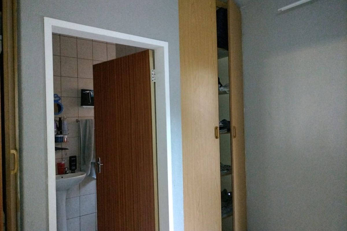 Bedroom featuring a built-in wooden wardrobe and an adjacent en-suite bathroom with a pedestal basin and tiled finishes.