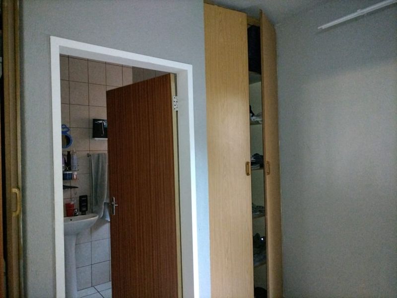 Bedroom featuring a built-in wooden wardrobe and an adjacent en-suite bathroom with a pedestal basin and tiled finishes.