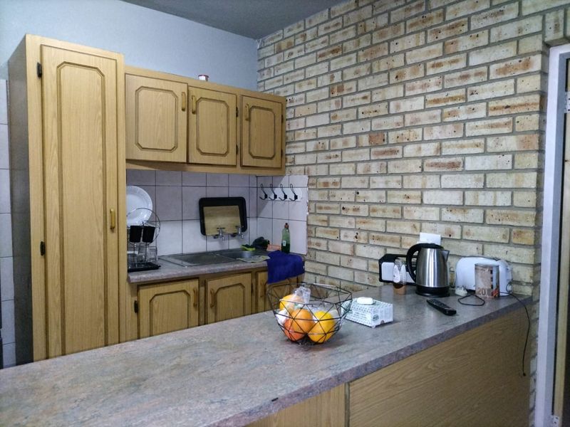 A functional kitchen featuring timber-look cabinetry, a durable laminate countertop, a tiled splashback, and a distinctive exposed brick feature wall.