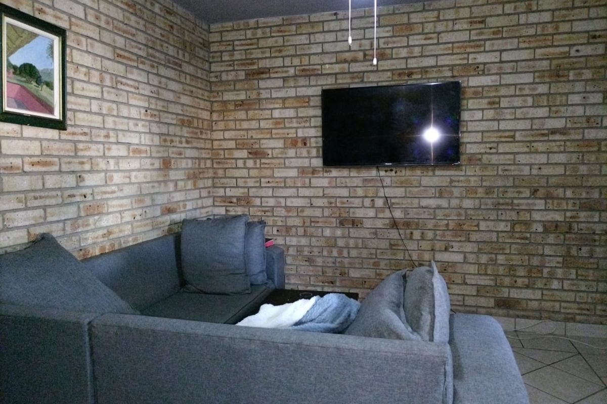 A living room featuring a prominent exposed brick feature wall, tiled flooring, and a ceiling fan.