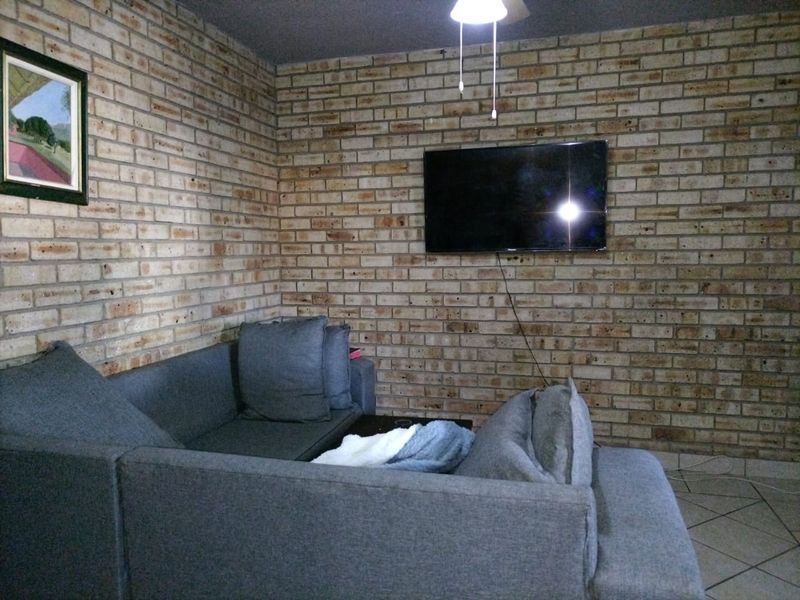 A living room featuring a prominent exposed brick feature wall, tiled flooring, and a ceiling fan.