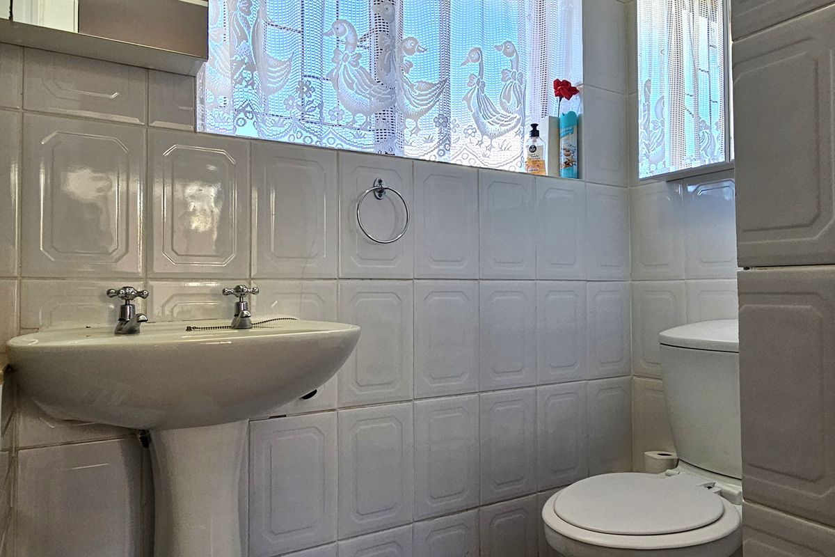 A functional bathroom featuring a pedestal basin, dual tap mixer, and toilet, finished with classic white wall tiling.
